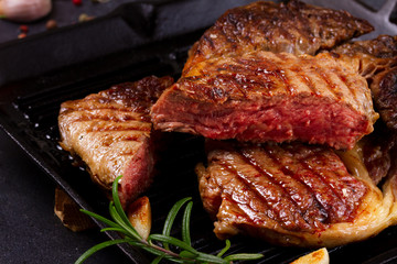 Grilled cut of beef steak in pan with spices on dark stone background