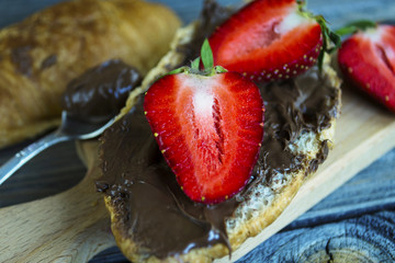croissant with chocolate pasta and strawberries on an old wooden background