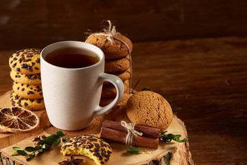 Christmas concept with a cup of hot tea, cookies and decorations on a log over wooden background, selective focus