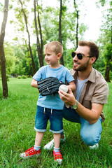 Fototapeta premium father hugging son with baseball ball and glove at park