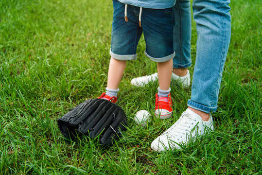 cropped image of father and son standing on grass near baseball ball and glove