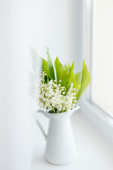 bouquet of fresh spring lilies of the valley in a white jug on the windowsill