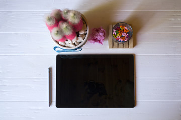 A tablet with stylus, pink cactus, crumpled sheet of paper and multicolored letters on a white...