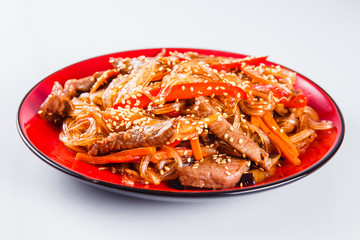 Noodles with  beef, pepper and sesame seeds on a red plate on a white background. Traditional Italian pasta. Close