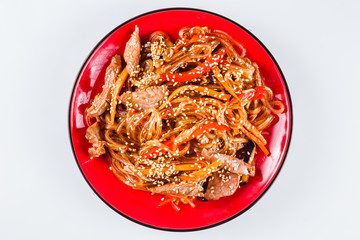 Noodles with  beef, pepper and sesame seeds on a red plate on a white background. Traditional Italian pasta. Close top view