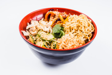 Noodles mix (chicken, pepper, cucumber and sesame seeds) on a red plate on a white background. Traditional Italian pasta. Close