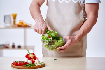Man cooking at kitchen making healthy vegetable salad, close-up, selective focus.