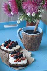Sandwiches with sweet cheese and berries, a cup of coffee in blue wooden background