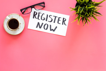 Membership concept. Template for registration. Register now hand lettering iconon word desk with glasses, coffee, plant on pink background top view space for text
