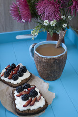 Sandwiches with sweet cheese and berries, a cup of coffee in blue wooden background