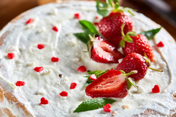 Tart with strawberries and whipped cream decorated with mint leaves on rustic wooden background, selective focus