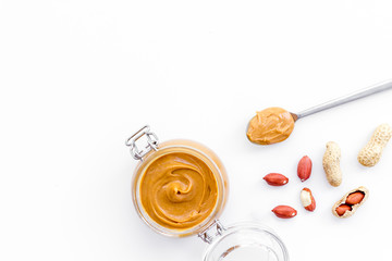 Peanut butter in glass jar near peanut on white background top view copy space