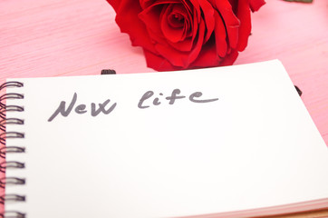 Notepad with new life inscription and red rose flower on purple background. Beginning of new life concept.