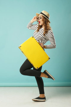 Young happy beautiful woman in hat and funny toy glasses holding yellow suitcase
