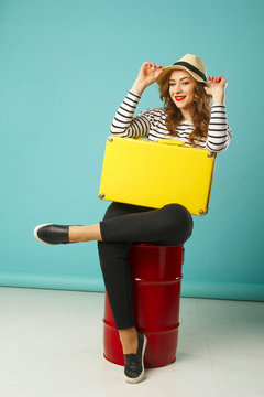 Young happy beautiful woman in hat holding yellow suitcase over blue background