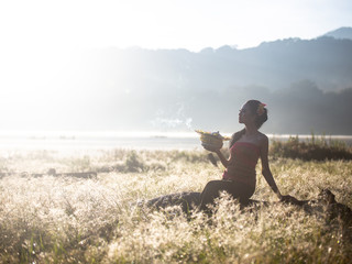 Bali girl poses while wearing traditional sarong in native pattern with nice lake in the background / travel concept / Indonesia /Rim light