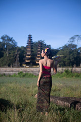 Bali girl poses while wearing traditional sarong in native pattern with nice landmark in the background / travel concept / Indonesia
