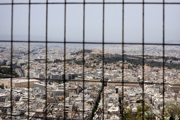 Obraz premium Greece, Athens: Skyline through fence with famous Acropolis, mass of houses, skyline, rooftops in the city center of Greek capital - concept urban development town planning structure living condition.
