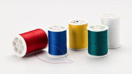 Five spools of sewing thread of different colors on a white surface