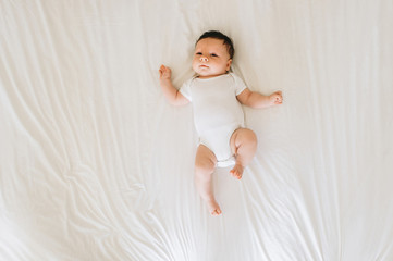 overhead view of cute newborn baby in white bodysuit lying on bed
