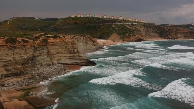 Aerial view from a surf spot with waves and a group of surfers in Ribeira d' Ilhas beach in Ericeira, Portugal