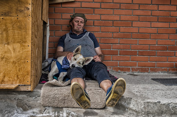 Two homeless fiends - man and dog sleeping while sitting on a concrete against brick wall