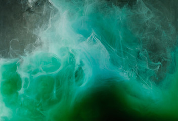 abstract flowing white, green and blue ink on black background
