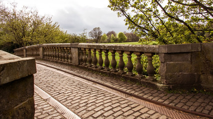 An ornate stone bridge and balustrade with cobblestone path.