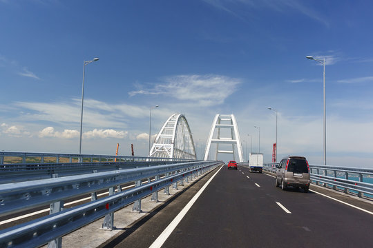 Fototapeta Cars on the Crimean bridge drive up to the white metal arches over the fairway