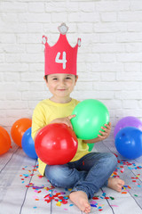 niño feliz con corona con el número 4 sosteniendo globos de colores