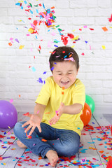 niño feliz lanzando confetti de colores rodeado de globos