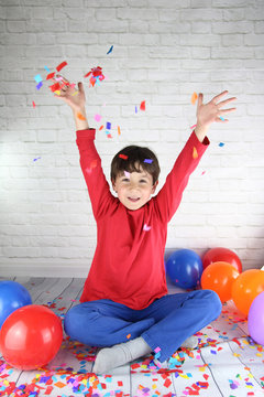 ni&ntilde;o feliz lanzando confetti de colores rodeado de globos