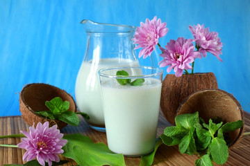 Coconut milkshake with mint flavour in a glass surrounded by coconut shells and pink flowers