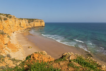 Atlantic Ocean sandy beach formed between two cliffs at sunset, Algarve, Portugal. Waves are rolling on an empty secluded sandy beach.