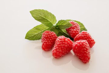 Fünf rote Himbeeren mit Minze auf weissem Hintergrund