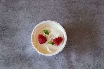 Zwei rote Himbeere und grüne Minze Blatt in Becher mit weissem griechischem Yougurt auf Beton Hintergrund