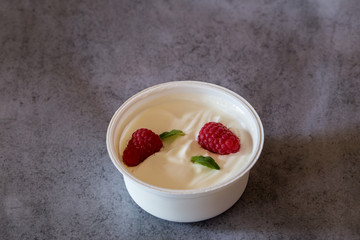 Zwei rote Himbeere und grüne Minze Blatt in Becher mit weissem griechischem Yougurt auf Beton Hintergrund