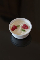 Zwei rote Himbeere und grüne Minze Blatt in Becher mit weissem griechischem Yougurt auf schwarzem Hintergrund