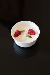 Zwei rote Himbeere und grüne Minze Blatt in Becher mit weissem griechischem Yougurt auf schwarzem Hintergrund