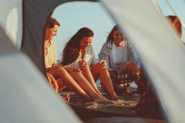 Naklejka premium Happy friends sitting on the beach singing and playing guitar during the sunset