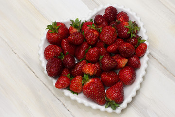 RIPE STRAWBERRIES ON A WHITE HEART PLATE AND WOODEN WHITE BACKGROUND