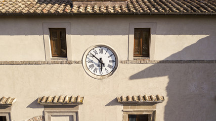Detail of a clock hanging on the facade of a building. The clock, belonging to the 800's, is located between two windows and continues to set the time and dictate the time to the town.