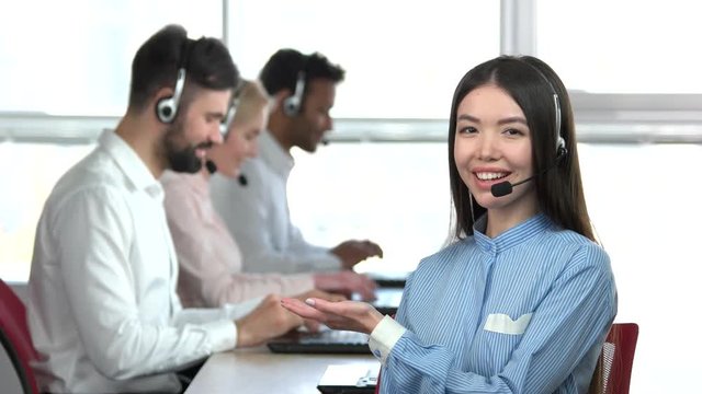 Female call center worker recommend her colleagues. Asian woman pointing at his colleagues co-workers.