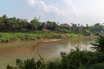 View of Nam Khan River and lush riverbank in Luang Prabang, Laos, on a sunny day.