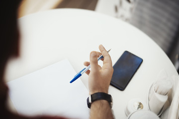 Young attractive man is writing note at the paper.