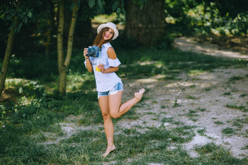 Fototapeta premium beautiful young girl in a park with a camera and juice in her hands
