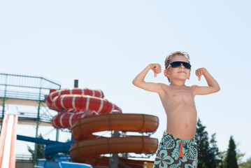healthy strong kid in sunglasses showing muscles in water park in summer day © ruslanshug