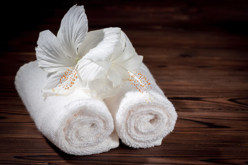 Obraz na płótnie Canvas spa concept of soft white cotton towels rolled and flowers of hibiscus on wooden texture, close up