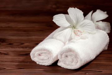 Obraz na płótnie Canvas spa composition of white cotton towels rolled and flowers of hibiscus on wooden background, close up