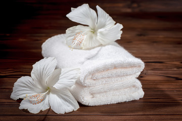 Obraz na płótnie Canvas spa concept of soft white cotton towels folded and flowers of hibiscus on wooden texture, close up